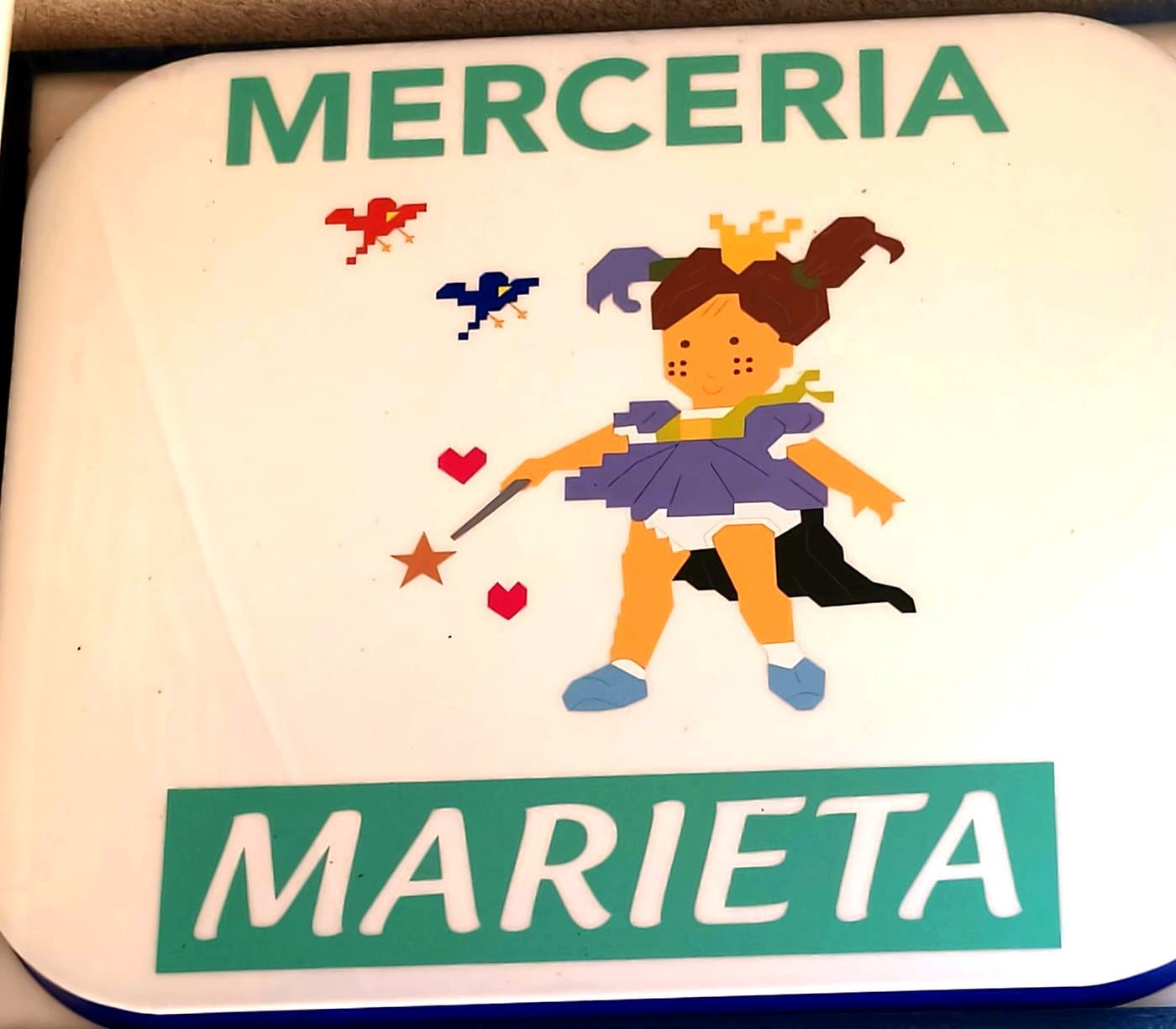 Cartel luminoso de Mercería Marieta con la muñeca, en la fachada de la tienda