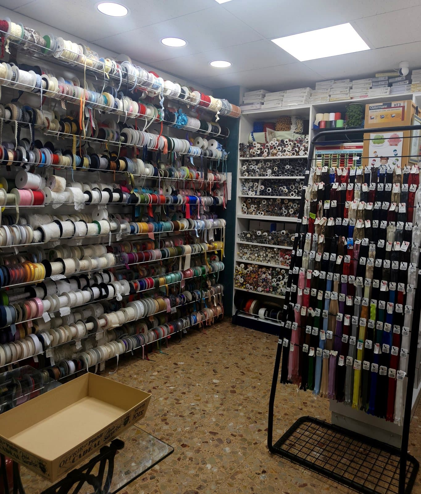 Pared de cintas de raso, terciopelo y puntillas en rollos, y expositor de cremalleras, en Mercería Marieta